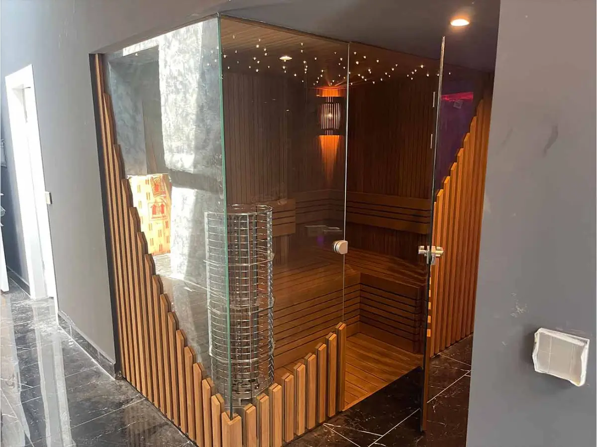 Glazed sauna cabin with thermo-wood benches, a cylindrical mesh tower heater, picket screen and a fibre-optic star ceiling