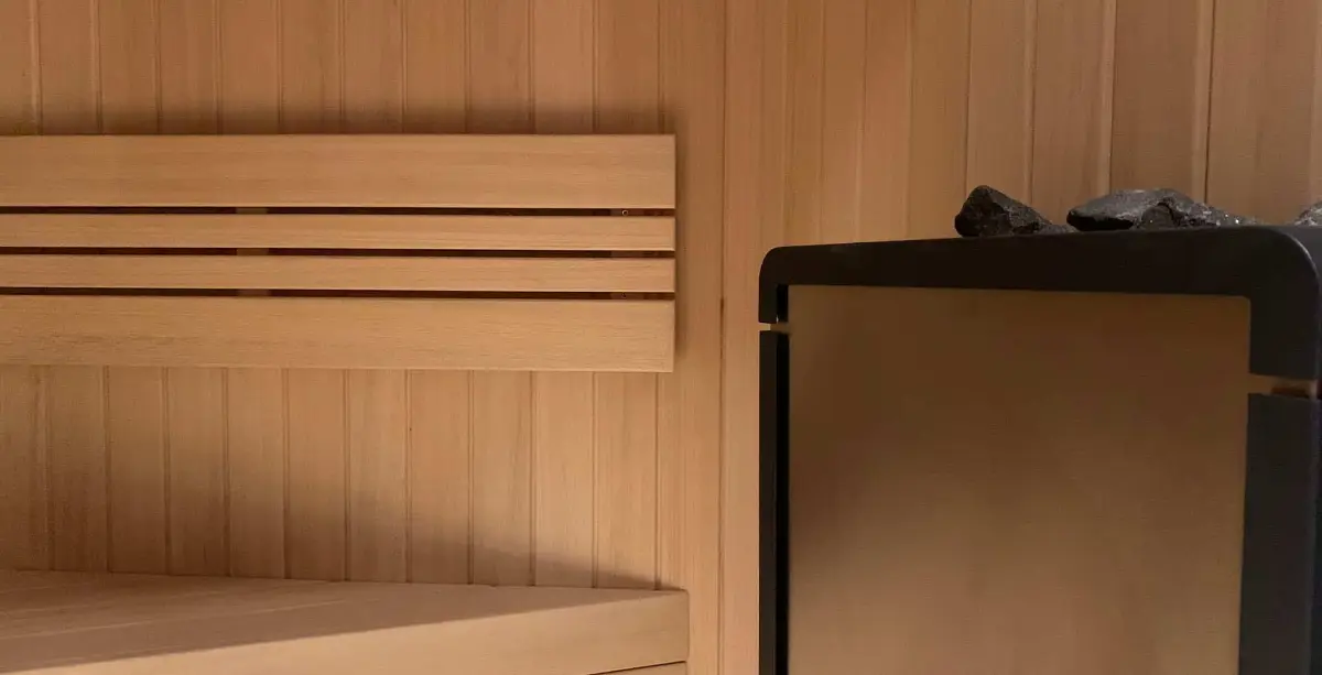 Sauna corner with pale timber panelling, slatted backrest and a stone-topped heater