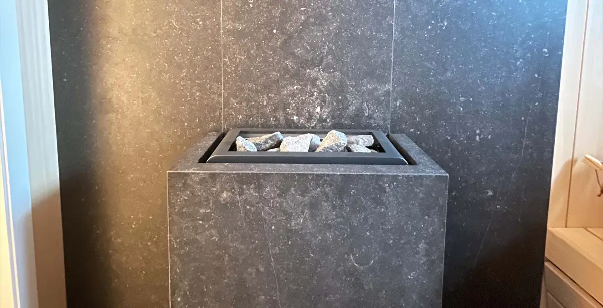 Dark stone-clad sauna heater with rough grey stones set in a tiled niche