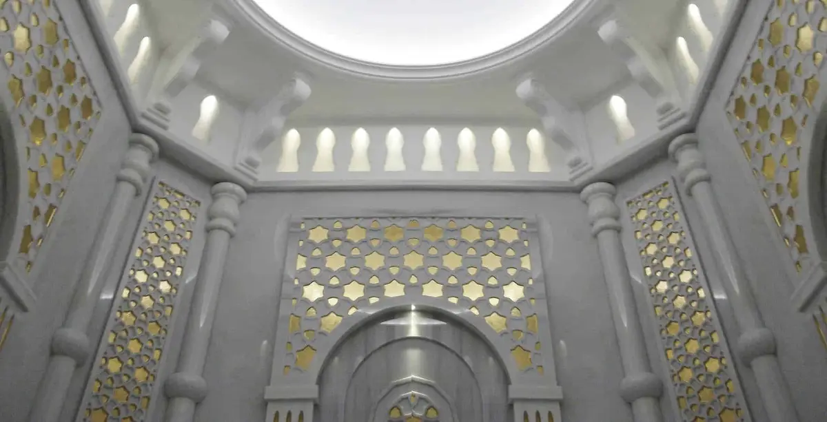 Carved white marble hammam with gilded pierced screens, slender columns and a domed ceiling oculus