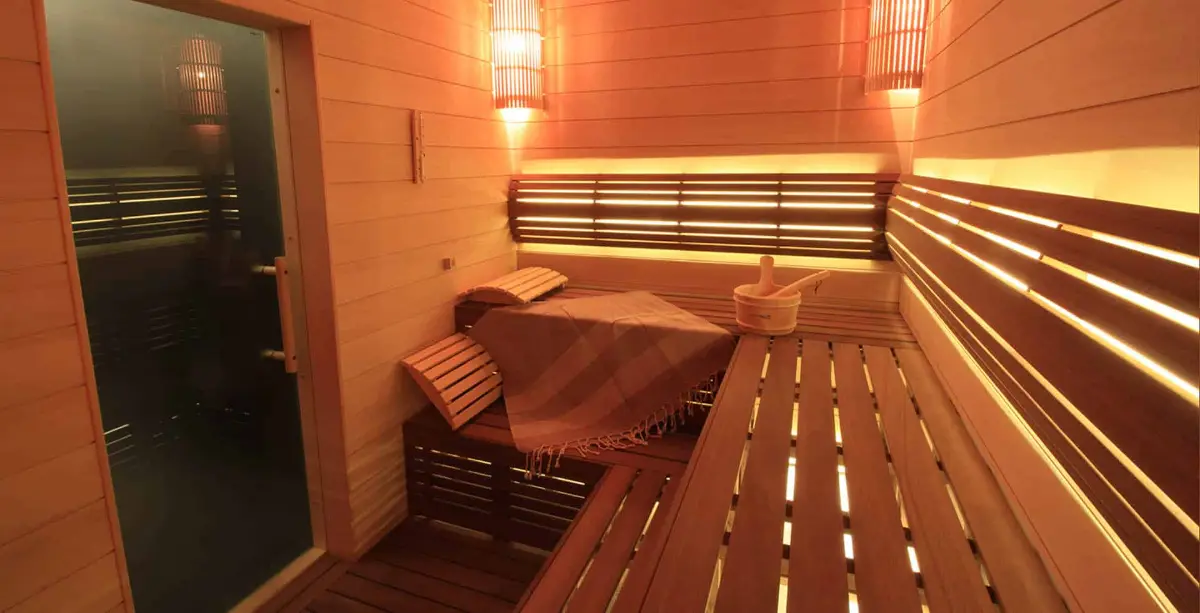 Warm wood sauna with backlit slat backrests, curved headrests, bucket, ladle and folded towel