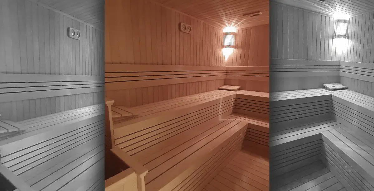 Light wood sauna with tiered corner benches, slatted backrest and a warm wall sconce