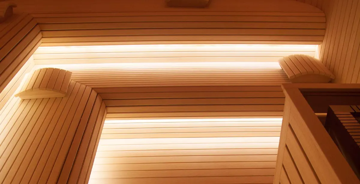 Upward view of a pale timber sauna showing curved headrests and glowing backrest light strips