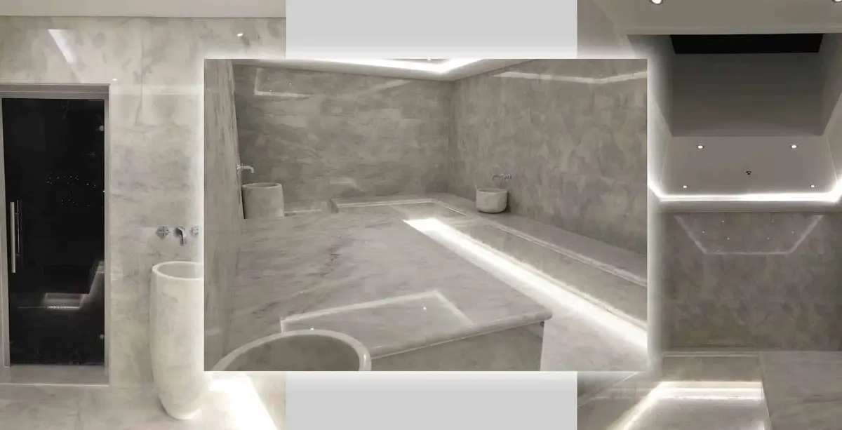 Grey marble hammam corner with heated platform, perimeter bench, round basins and recessed strip lighting