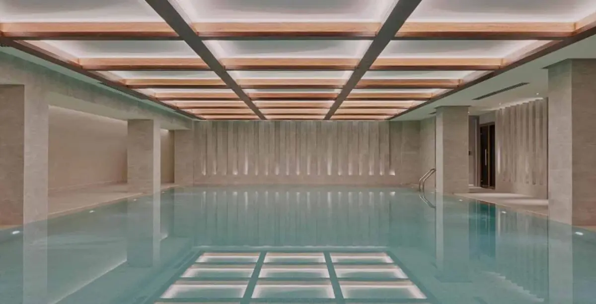 Indoor pool under a timber coffered ceiling with fluted stone walls and lit floor panels