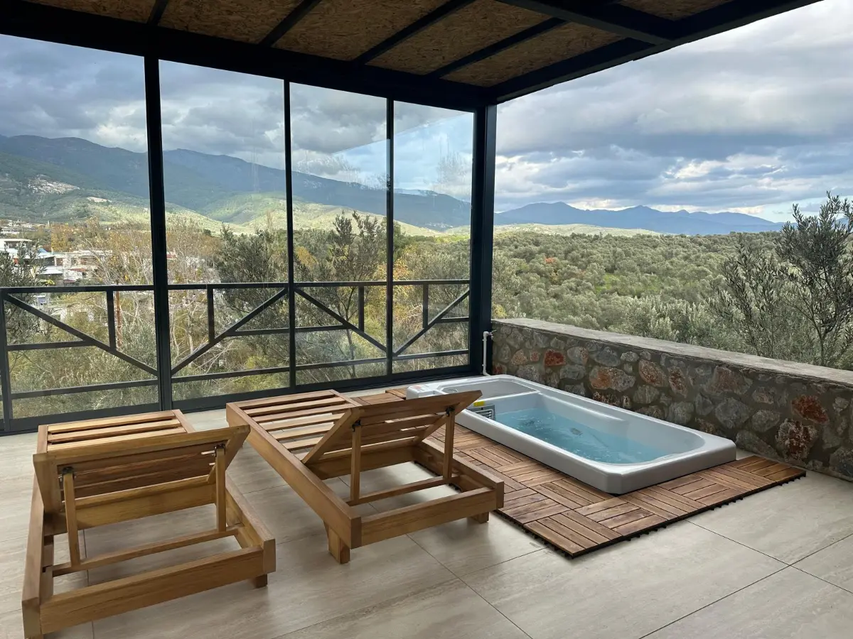 Water-filled sunken tub on a timber deck inside a glazed terrace with mountain views