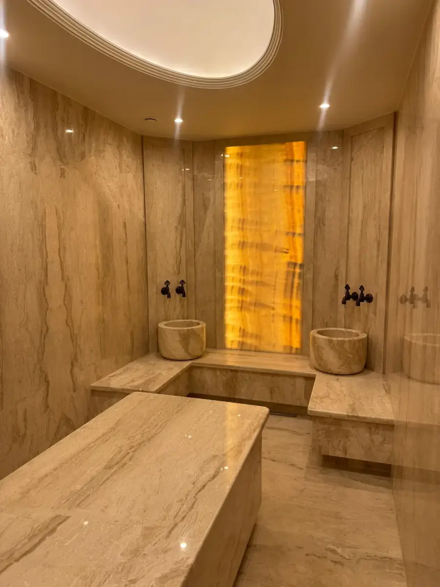 Private villa hammam with a marble massage slab, kurna basins and a backlit onyx feature panel