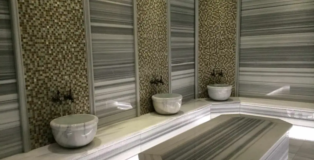 Hammam wall of striped marble and gold mosaic strips with three carved basins and brass taps
