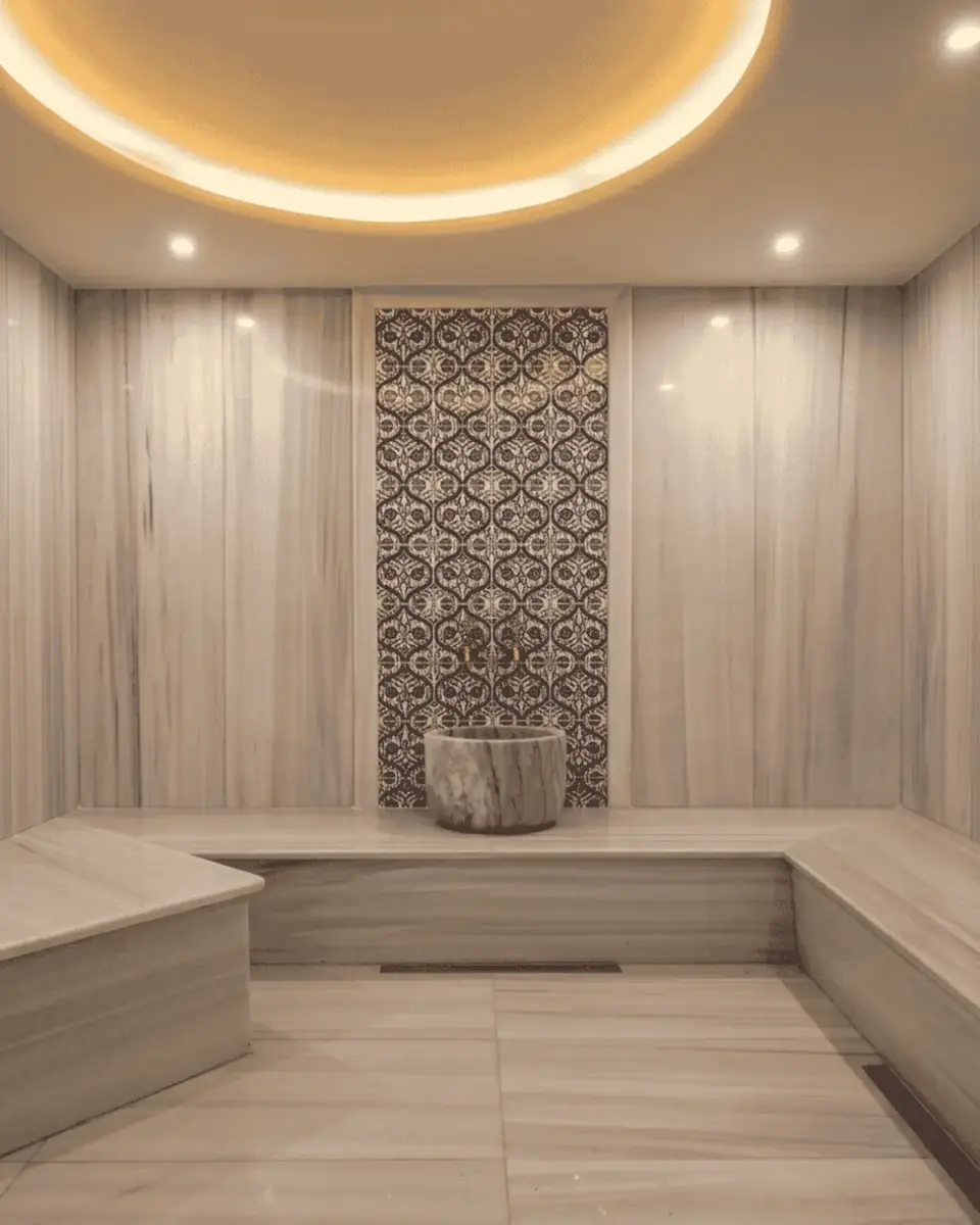 Hammam with pale marble walls, a patterned tile panel and a marble bowl on a pedestal