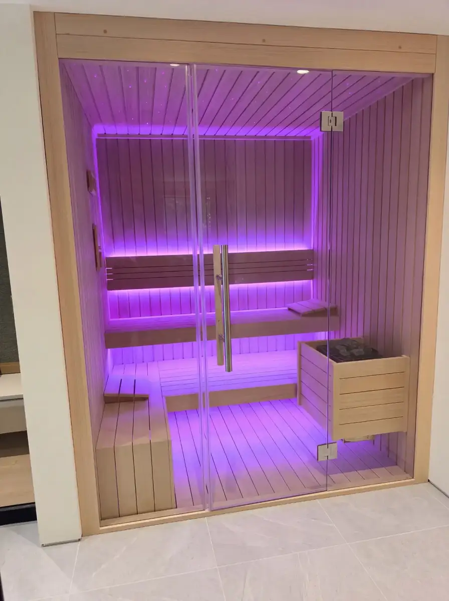 Glass-fronted home sauna lit in violet LED with tiered benches and a wood-clad heater guard