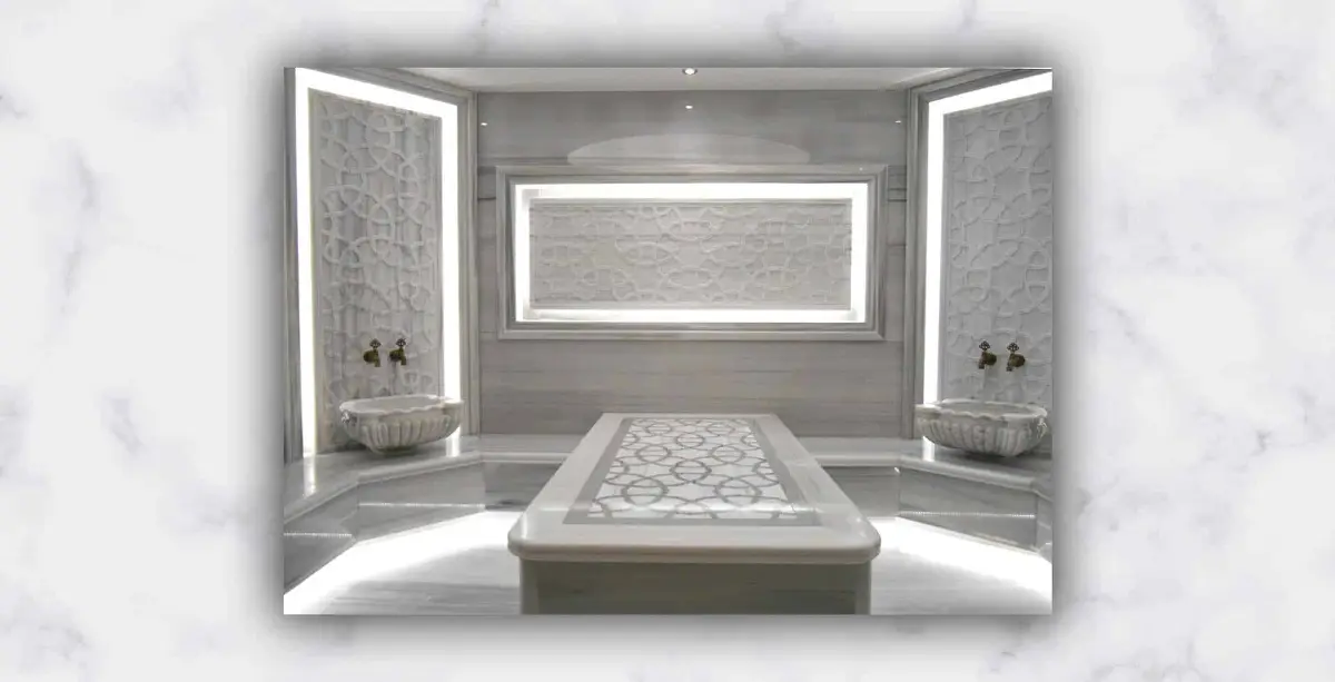 White marble hammam with backlit carved lattice panels, two wall basins and a patterned navel stone